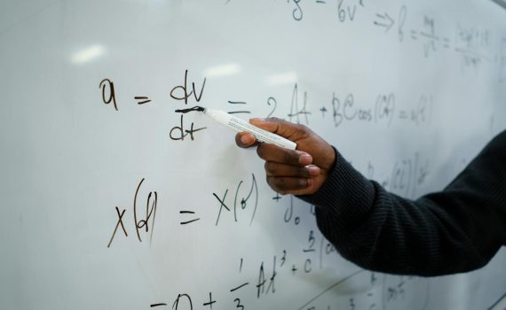 Close-up of hand writing equations on a whiteboard in a classroom setting.