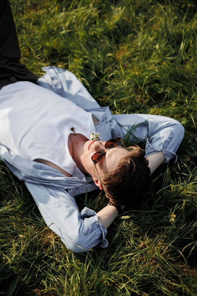 Man wearing sunglasses relaxing in a sunny field, enjoying a leisure moment outdoors.